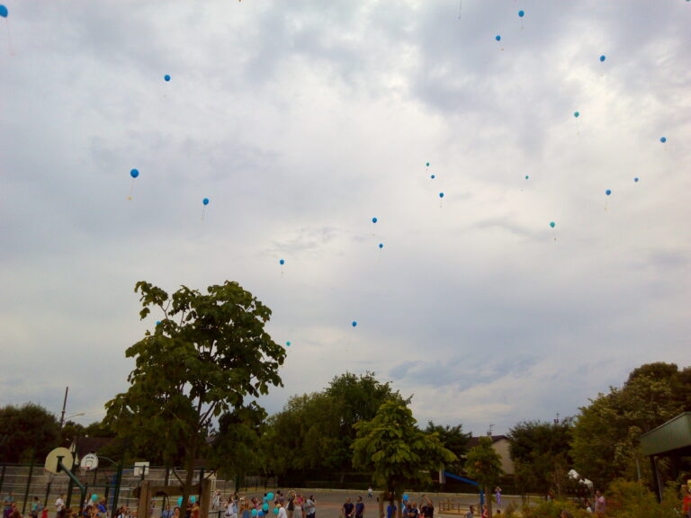 une vingtaine de ballons bleues qui s'envolent dans les airs au dessus d'une cours d'école avec des enfants