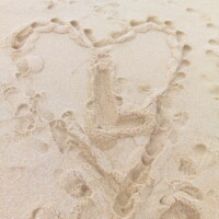 Un coeur dessiné dans le sable avec un L au milieu