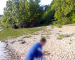 Photo d'une personne agenouillé sur un plage sur le bord d'un lac qui semble sortir d'un bateau et découvrir cette plage