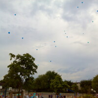une vingtaine de ballons bleues qui s'envolent dans les airs au dessus d'une cours d'école avec des enfants